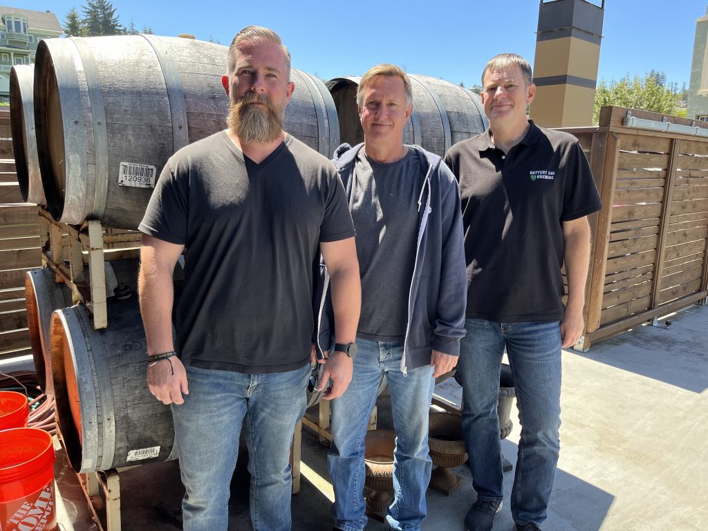 Battery 245 Brewing Co. founders Jonathan Elliott, Michael Ljungberg, and Jeff Kilday standing in front of barrels